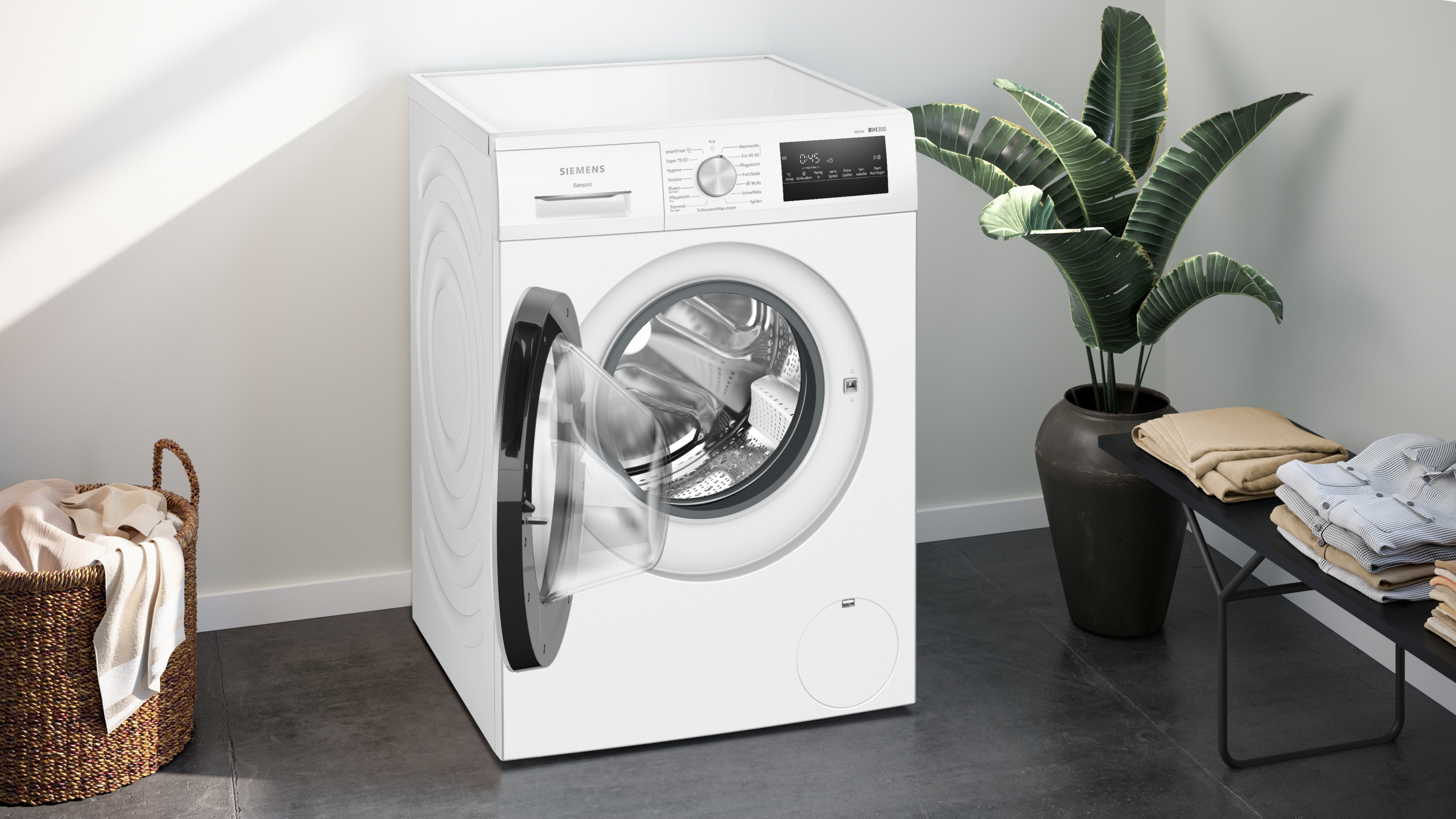 Weiße Siemens Waschmaschine mit offener Tür, daneben ein Wäschekorb und Pflanzen.