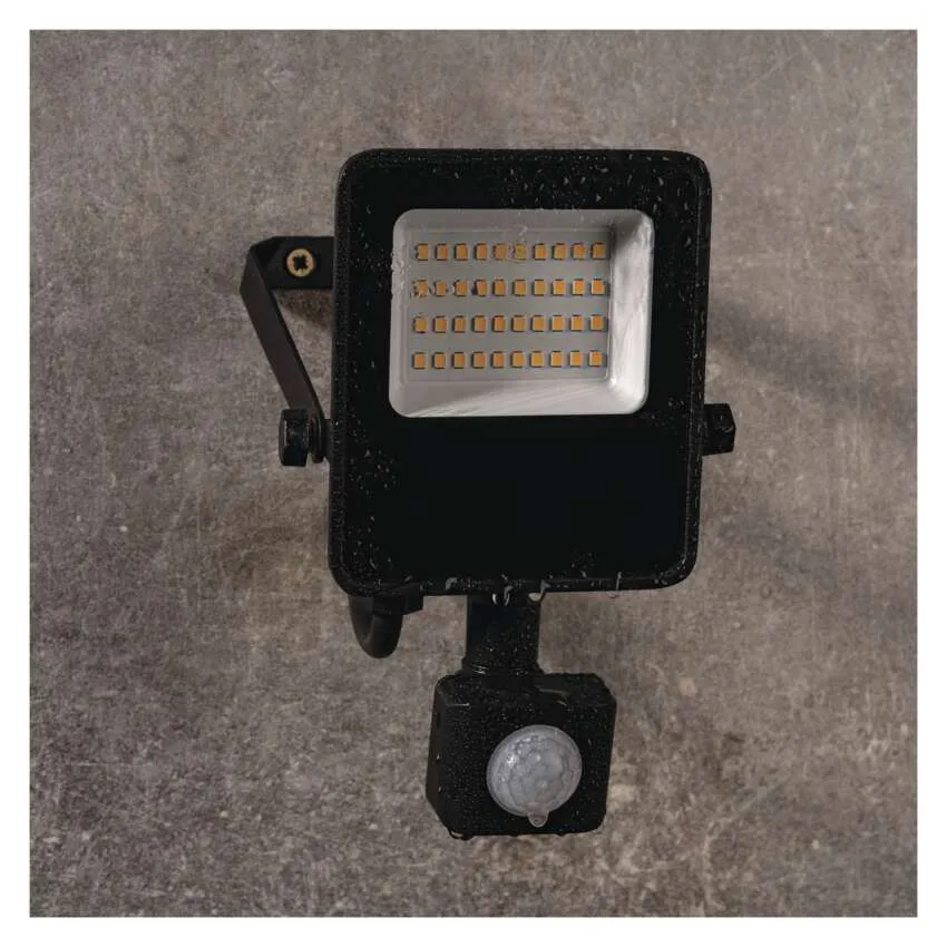 Egy fekete LED-es reflektor mozgásérzékelővel szürke falra van szerelve.
