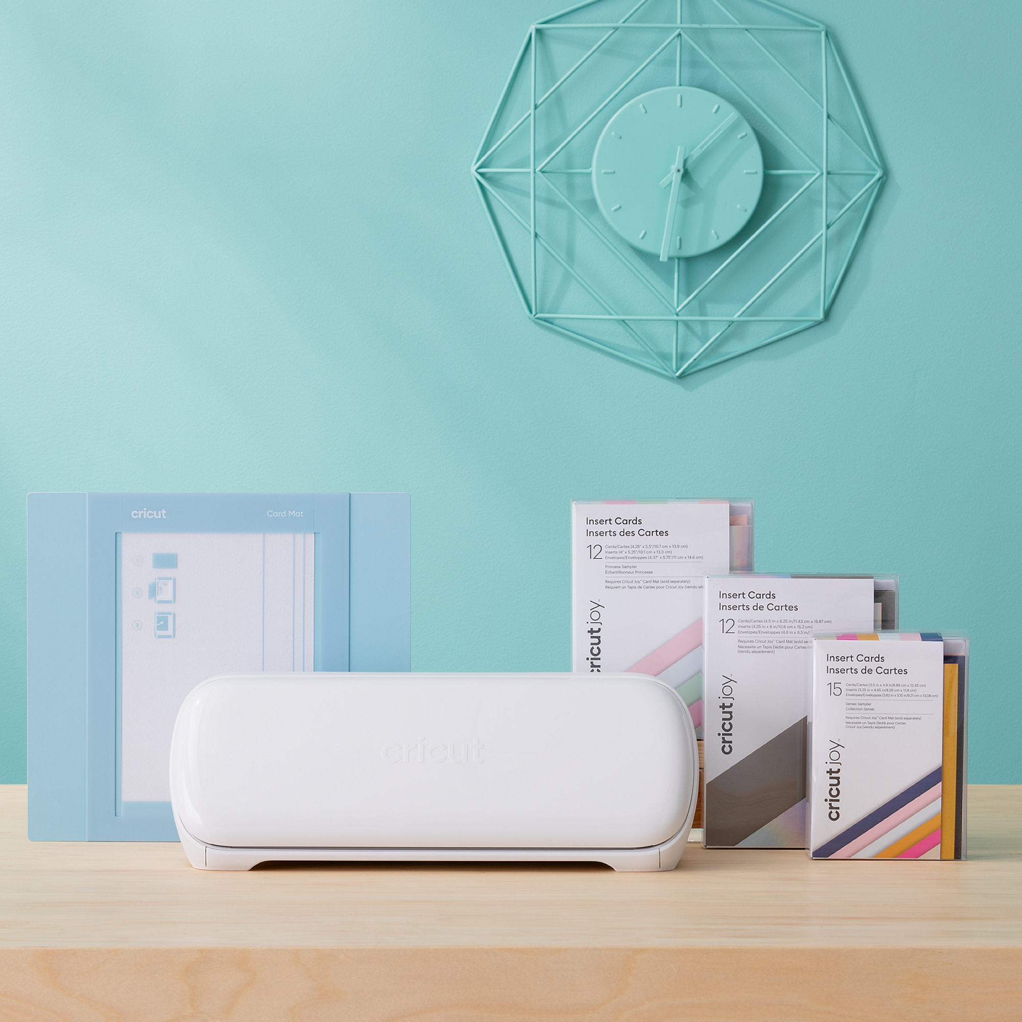 Una máquina blanca Cricut Joy, tapete para tarjetas azul y paquetes de insertos para tarjetas sobre una mesa de madera.