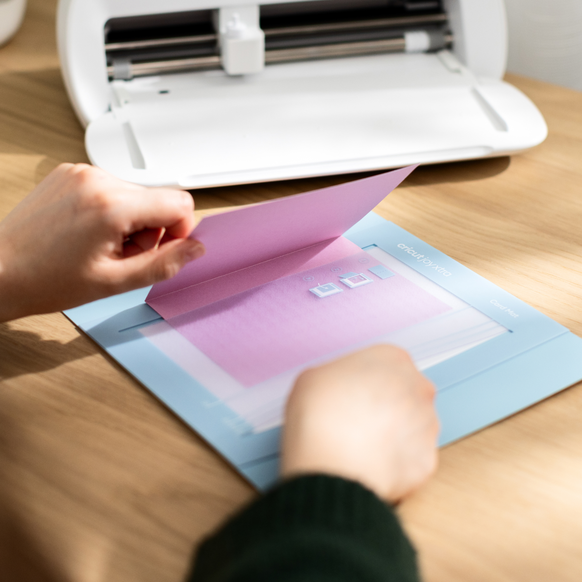 Persona coloca tarjeta rosa sobre tapete azul frente a máquina Cricut Joy Xtra.
