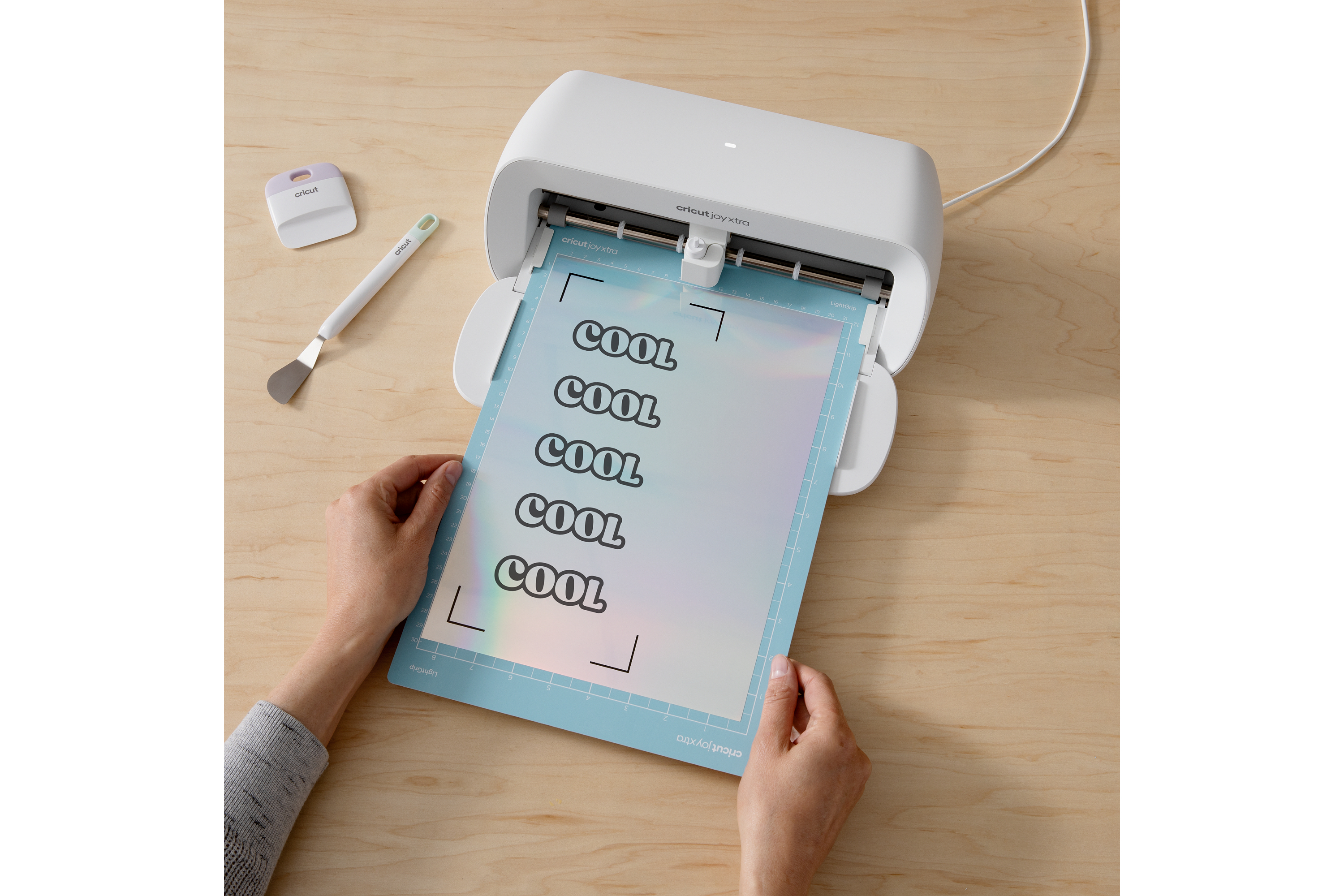 Una persona coloca una hoja con "COOL" en una máquina Cricut Joy Xtra blanca.