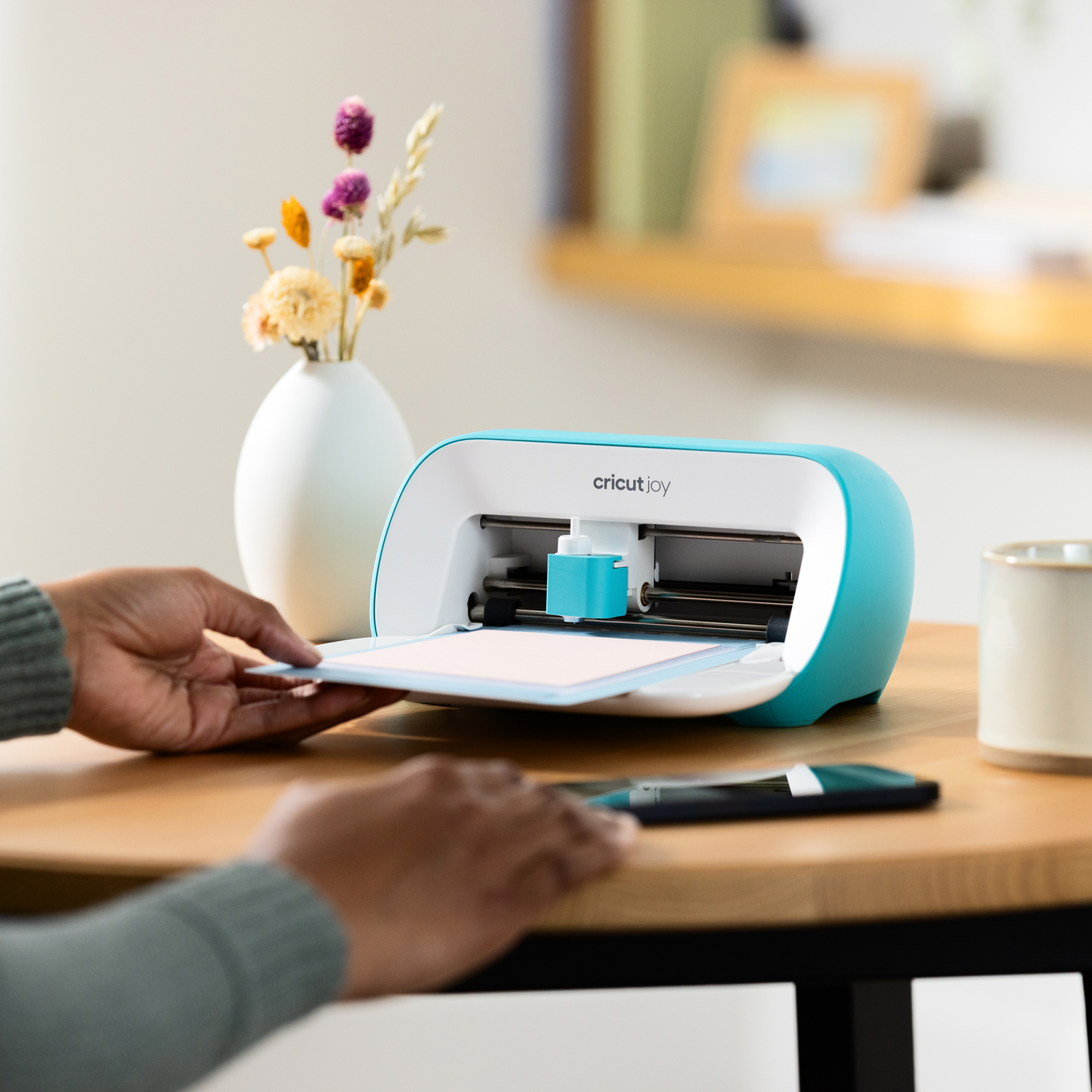 Una persona coloca una alfombrilla en una máquina de corte Cricut Joy turquesa.