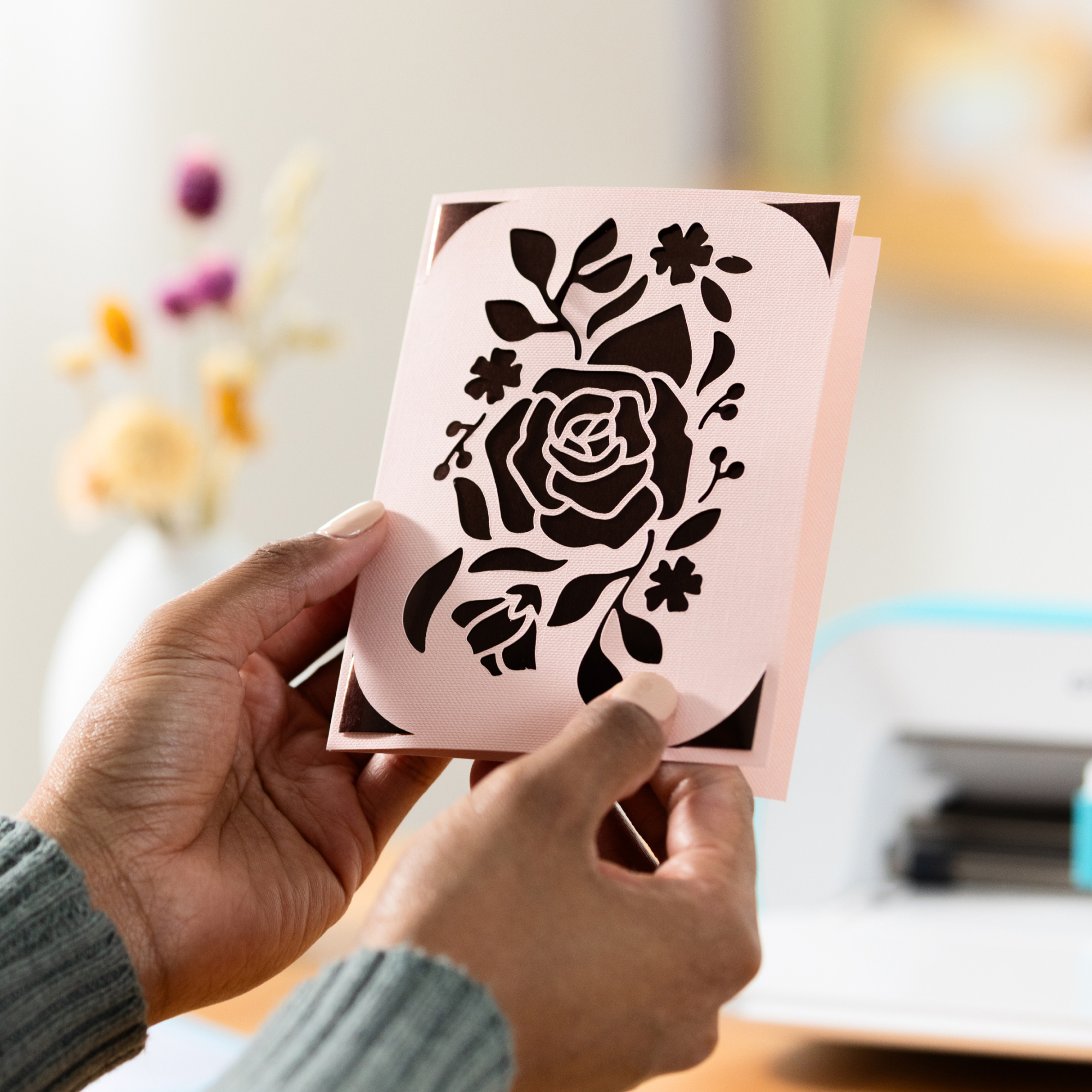 Una persona sostiene una tarjeta rosa con un diseño de rosa recortado.