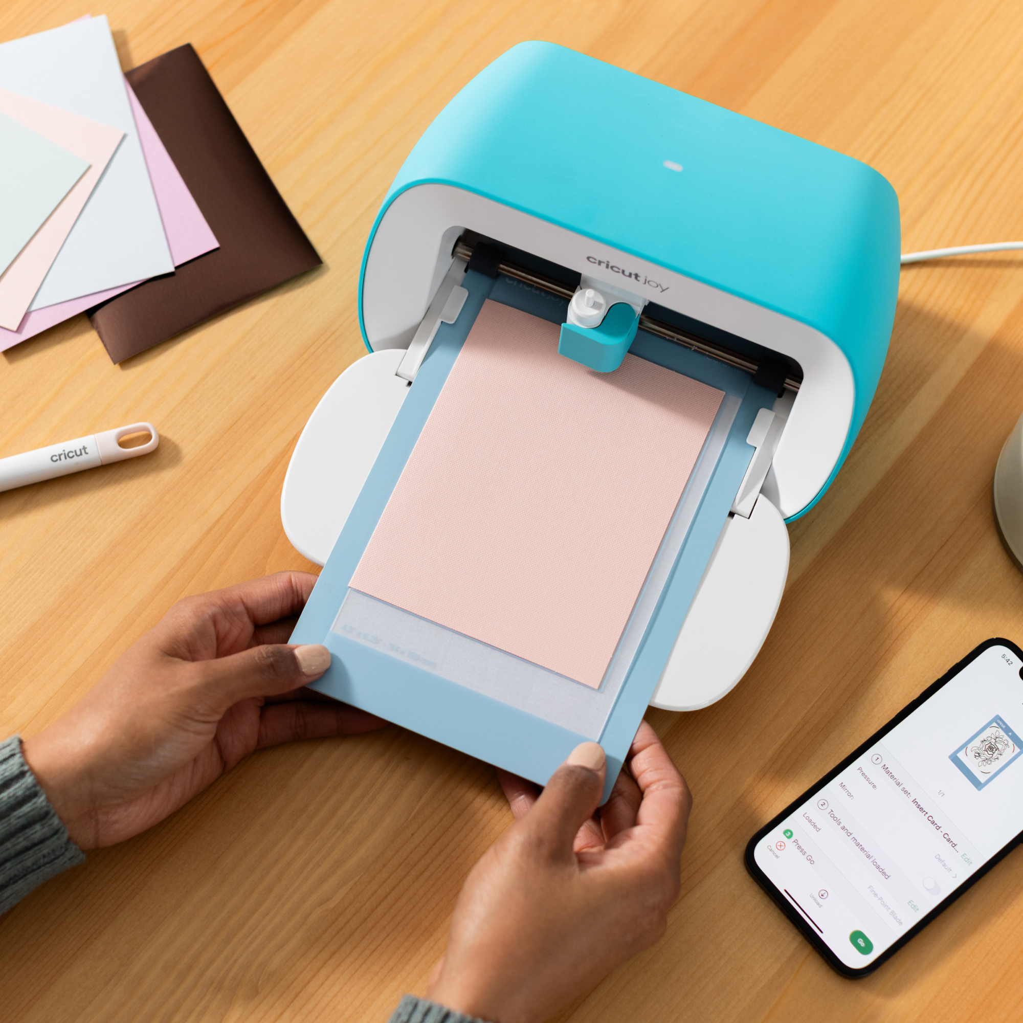 Una persona inserta una tarjeta rosa en una máquina de corte Cricut Joy de color verde azulado.