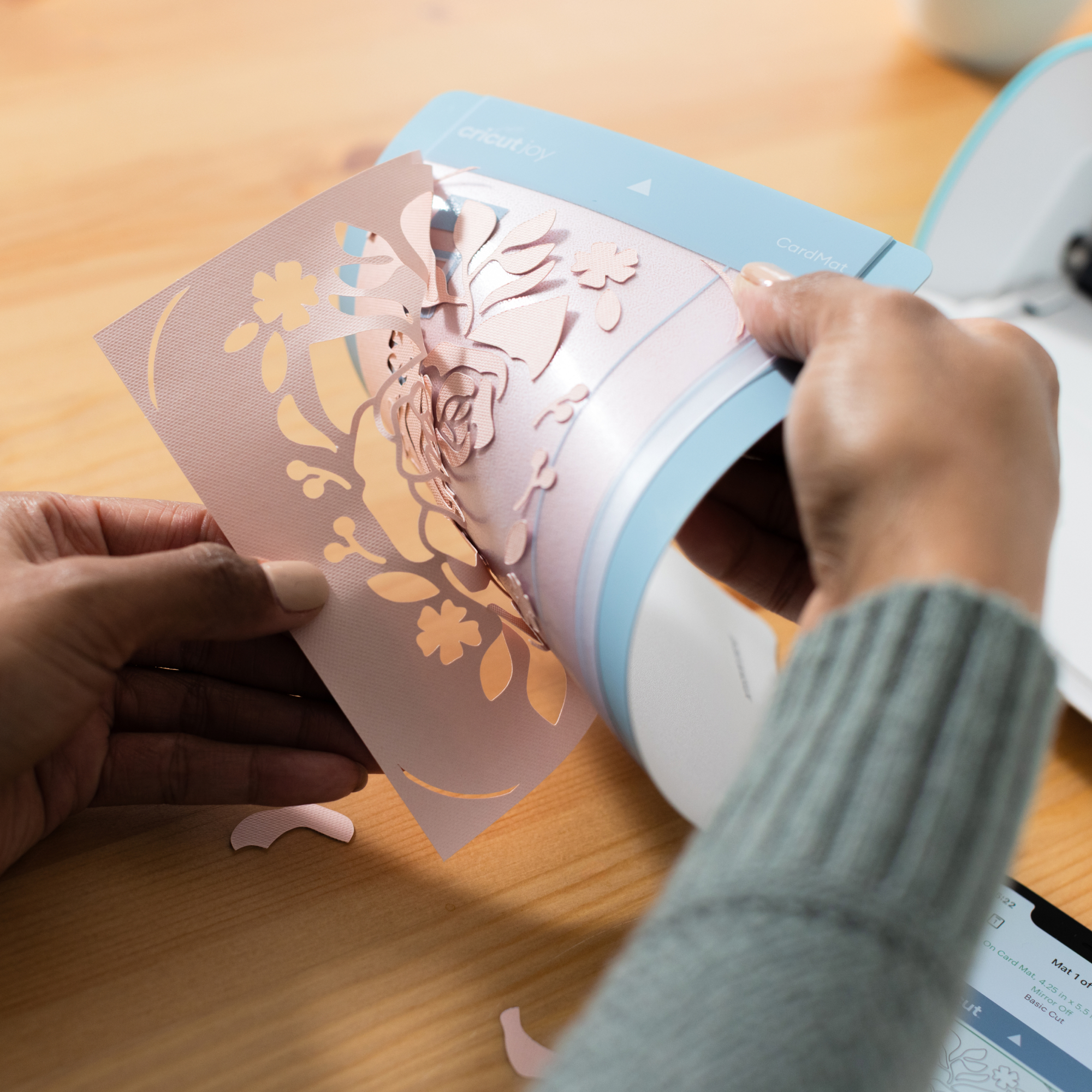Manos pelan una tarjeta rosa con flores recortadas de una Cricut CardMat.