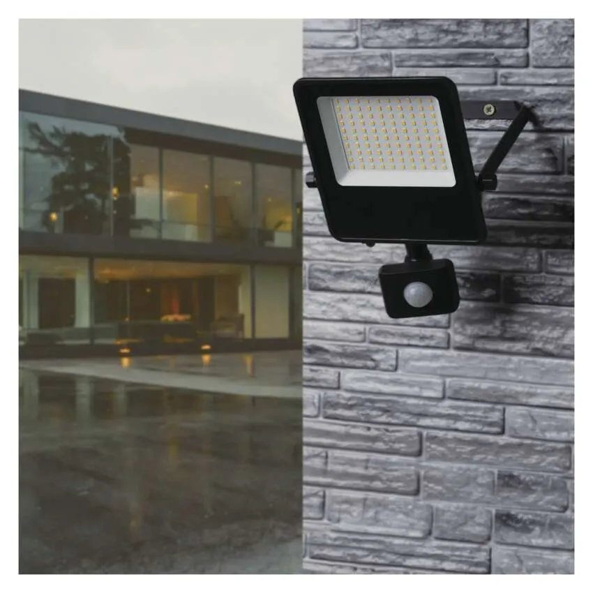 Fekete LED-es reflektor mozgásérzékelővel téglafalon, egy modern ház mellett.