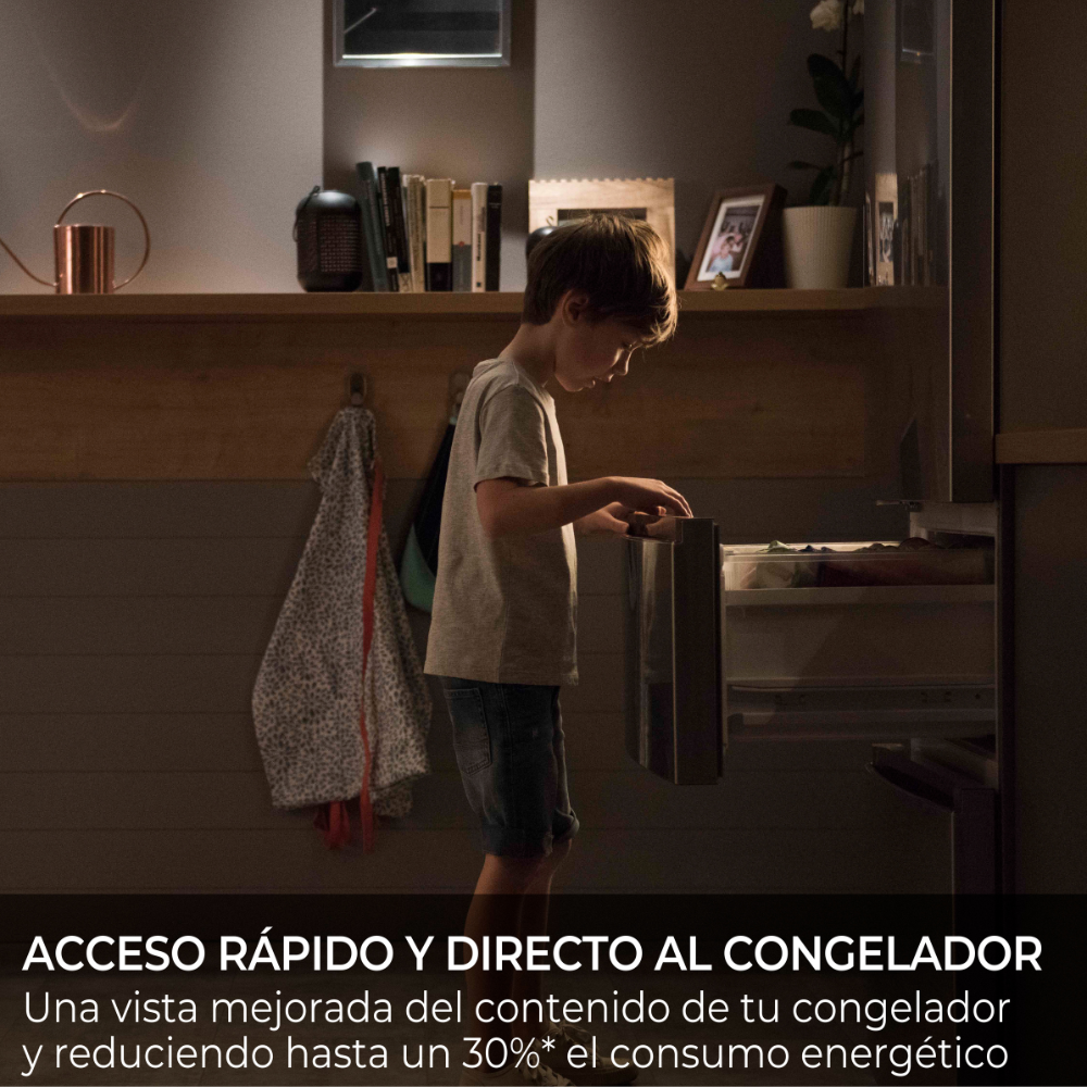 Un niño mete la mano en un congelador abierto, libros en el estante.