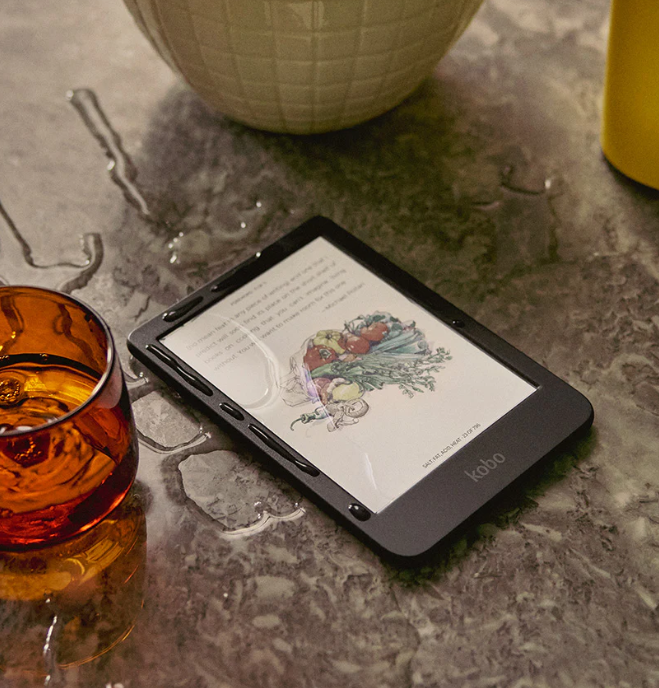 Czytnik e-booków z warzywami na ekranie, obok szklanki i plam wody.