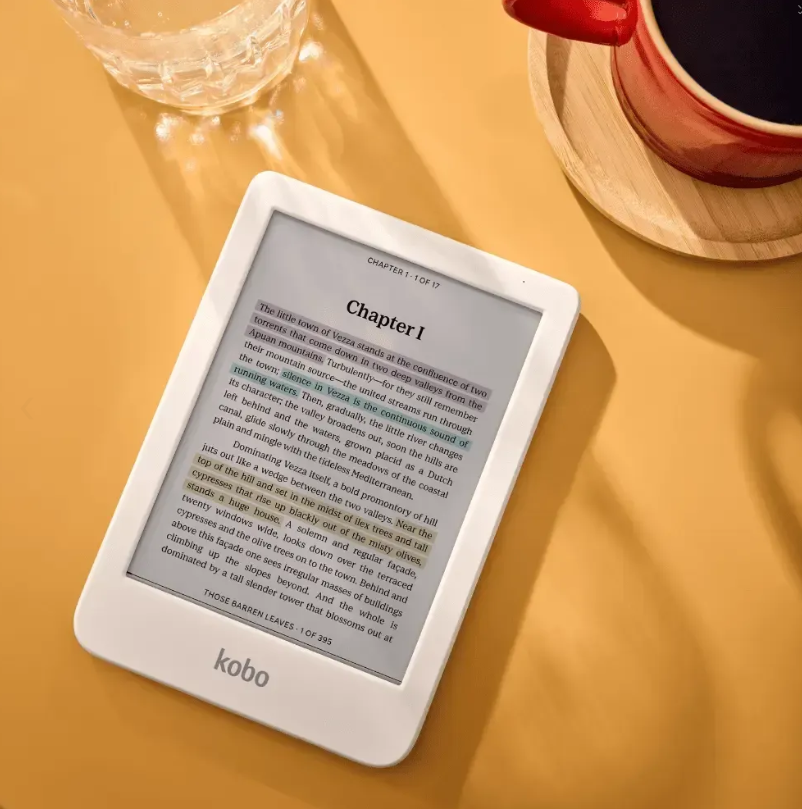 Czytnik e-booków leży na żółtym stole obok filiżanki kawy i szklanki wody.