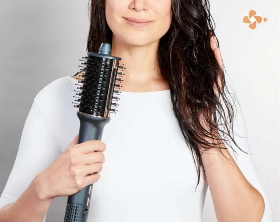 Kobieta z mokrymi włosami trzyma obrotową suszarkę do włosów w białej bluzce.