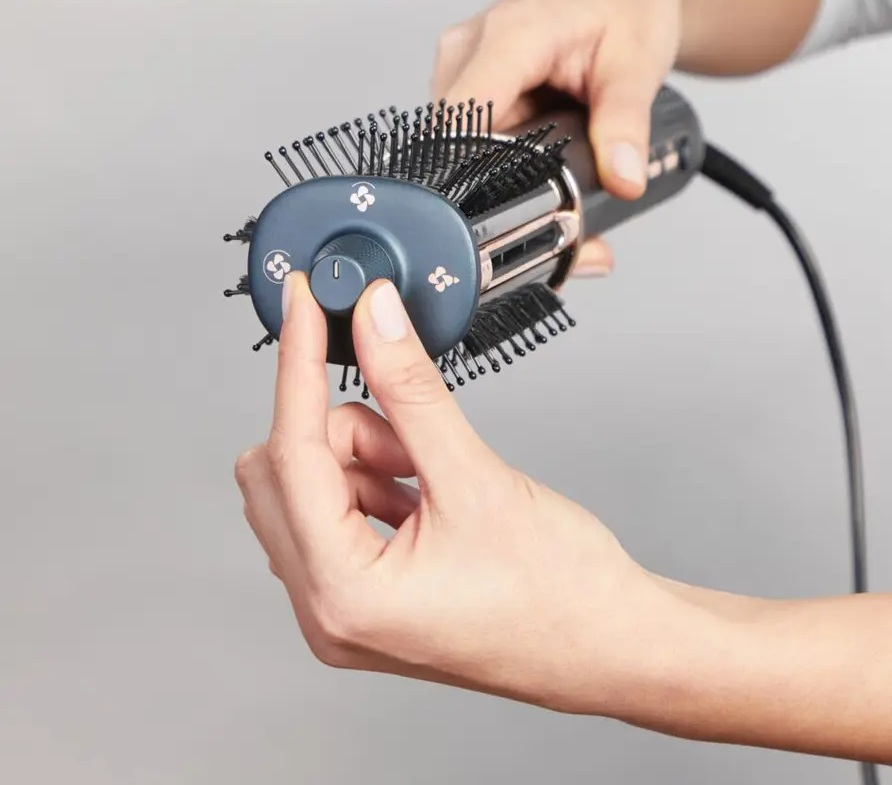 Ręka reguluje pokrętło na obrotowej głowicy szczotki suszarki.