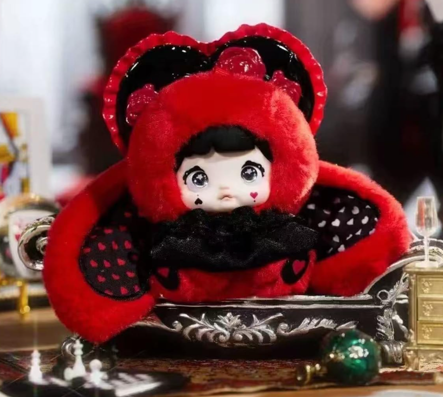 Eine Puppe in rotem Outfit mit Herzmotiv auf einer schwarzen Couch.