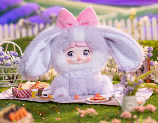 Ein flauschiges lila Kaninchen-Plüschtier mit pinker Schleife sitzt auf einer Picknickdecke.