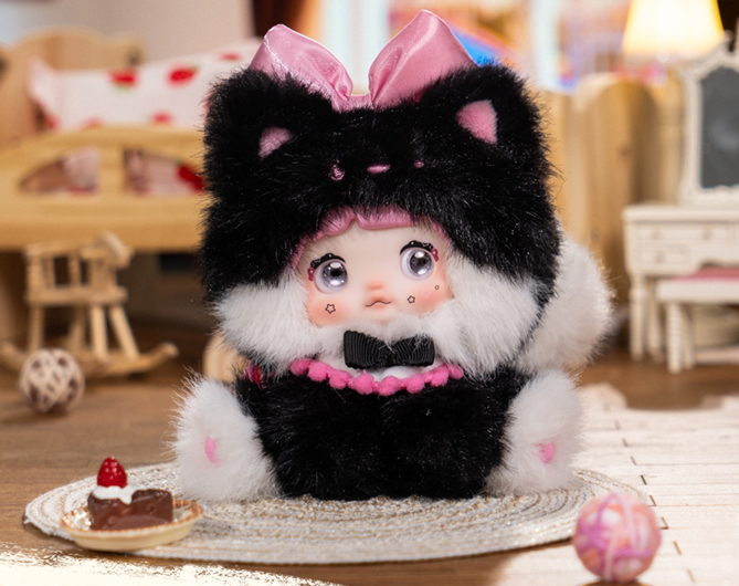 Ein Plüschtier mit Katzenohren und pinker Schleife sitzt auf einem Teppich mit Kuchen.