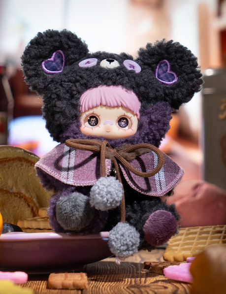 Eine Stoffpuppe in einem Bärenkostüm mit lila Herzen und Pompons.