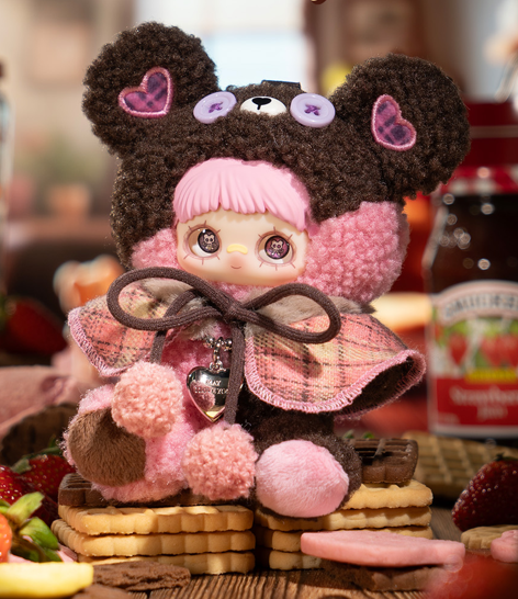 Eine Puppe im Bärenkostüm sitzt auf Keksen. Erdbeeren und Marmelade im Hintergrund.