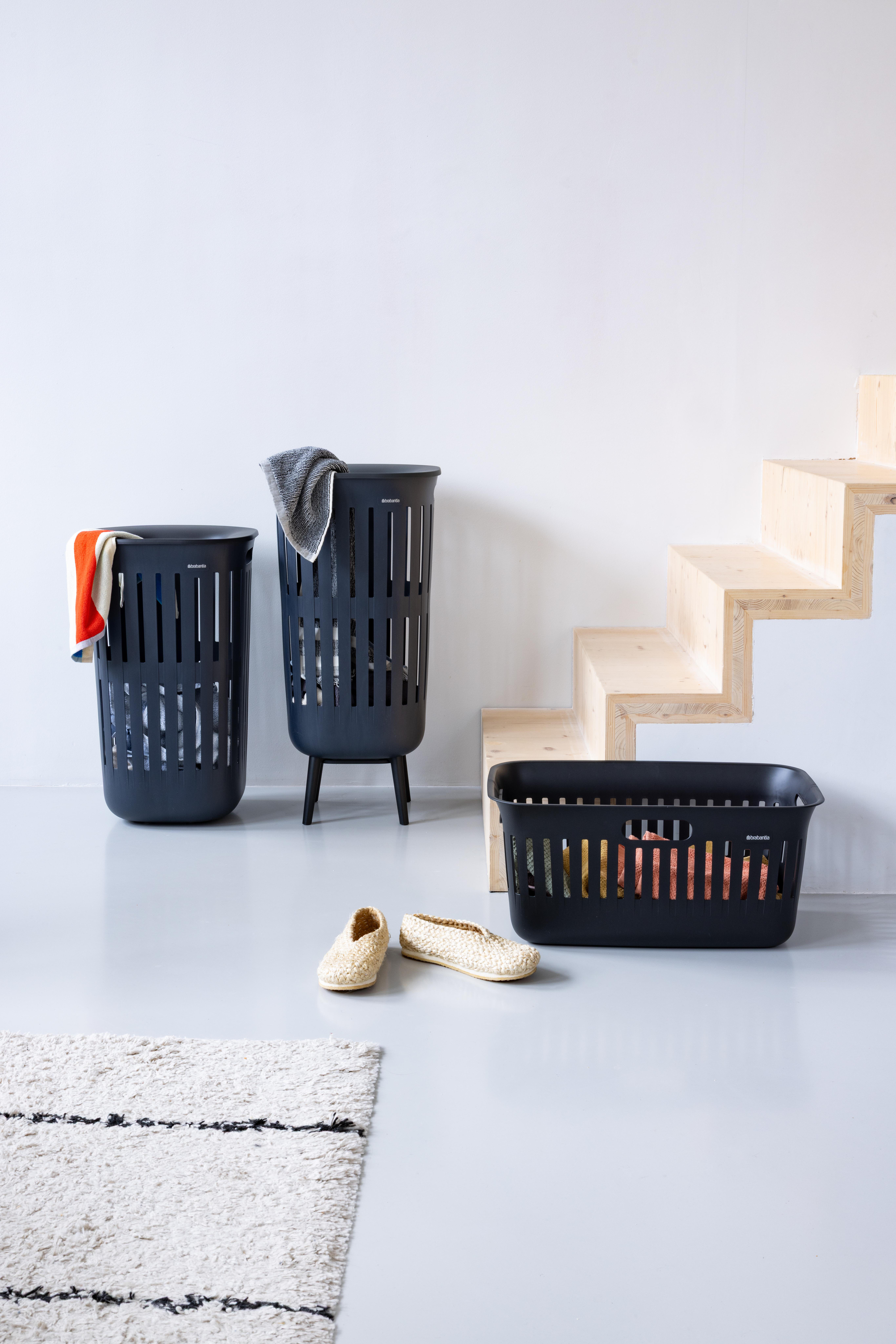 Drei schwarze Wäschekörbe, ein Teppich, zwei Hausschuhe und eine Holztreppe.