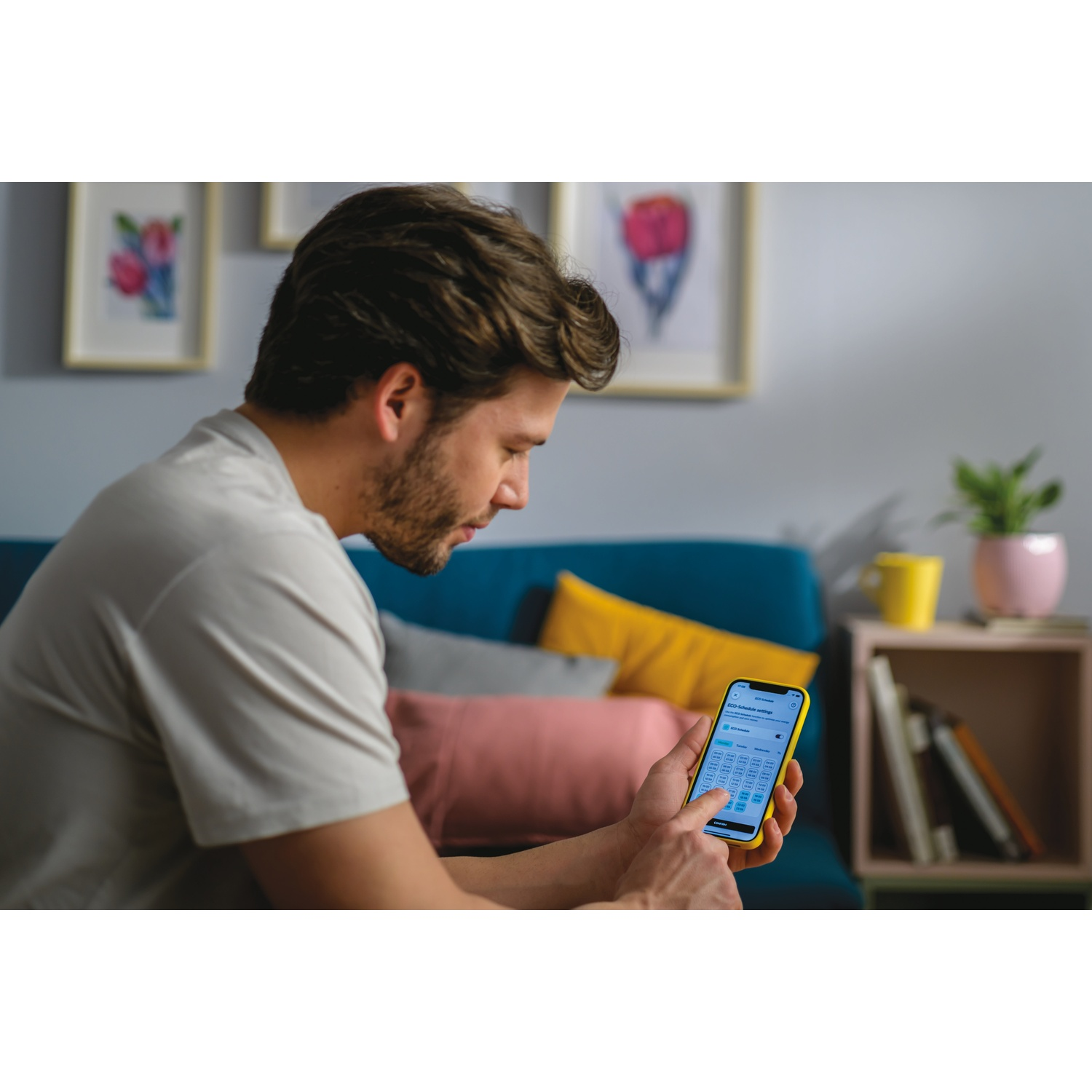 Uomo che tiene smartphone con app di pianificazione. Divano e quadri sullo sfondo.