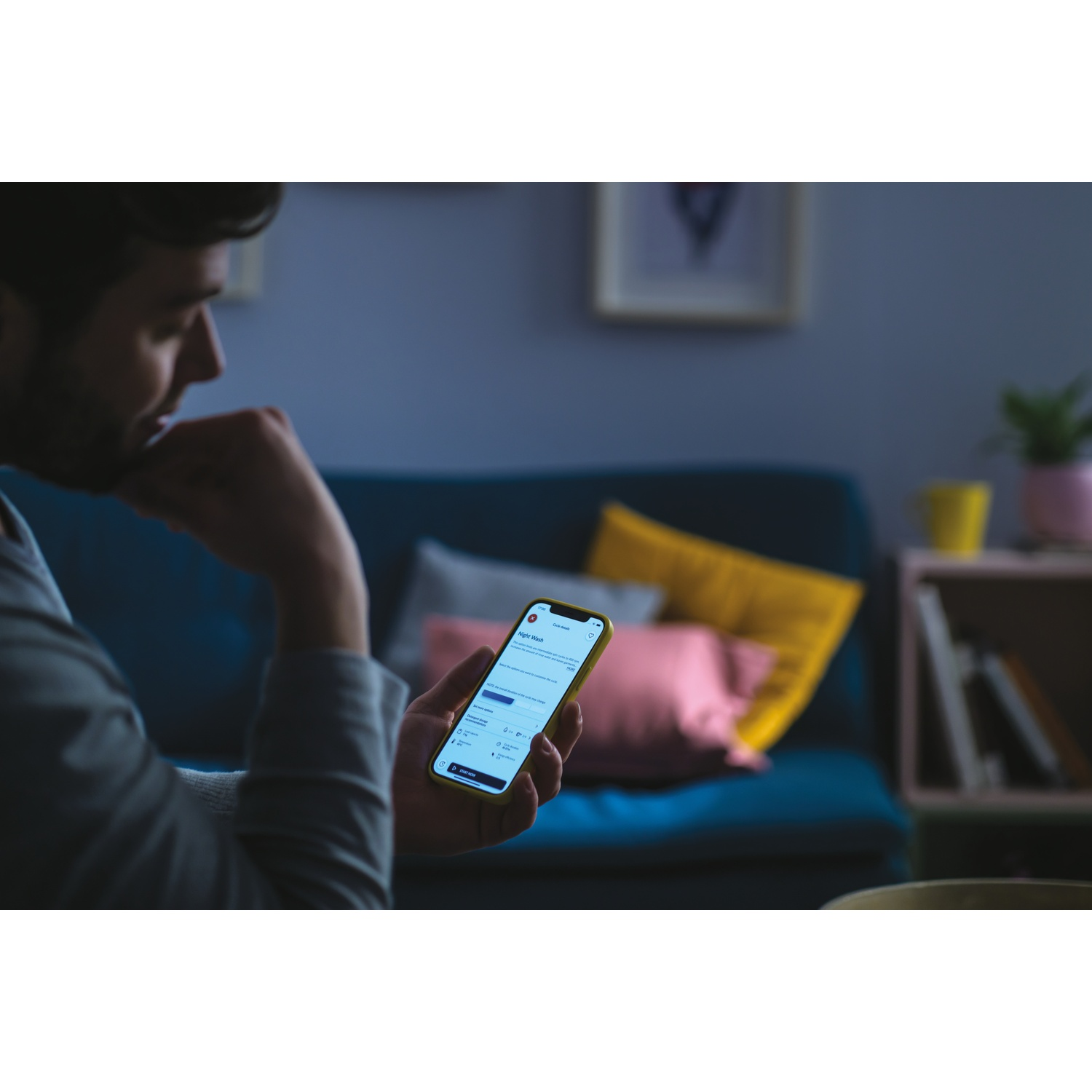 Uomo tiene uno smartphone con app lavatrice. Divano sullo sfondo.