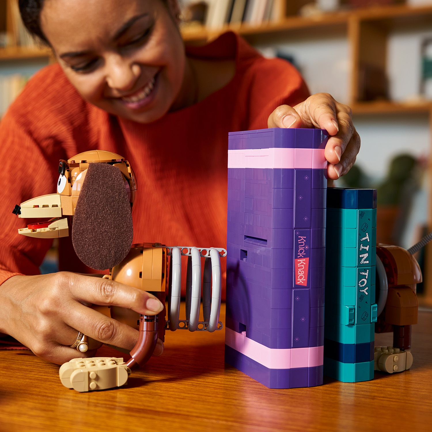 Donna costruisce un cane Lego marrone accanto a libri Lego viola e turchese.