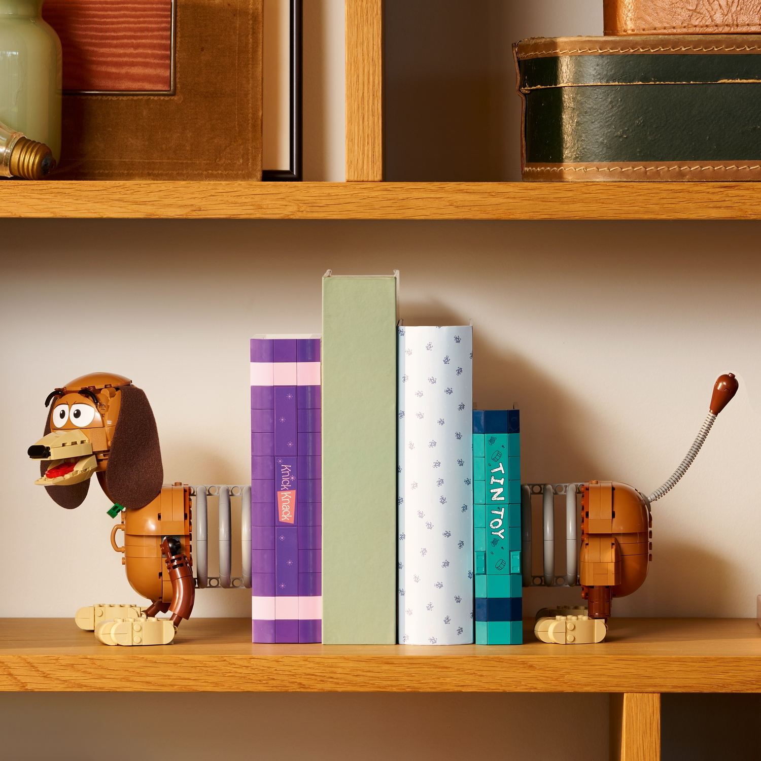 Un giocattolo Slinky Dog regge libri su uno scaffale di legno. Sono visibili altri oggetti.