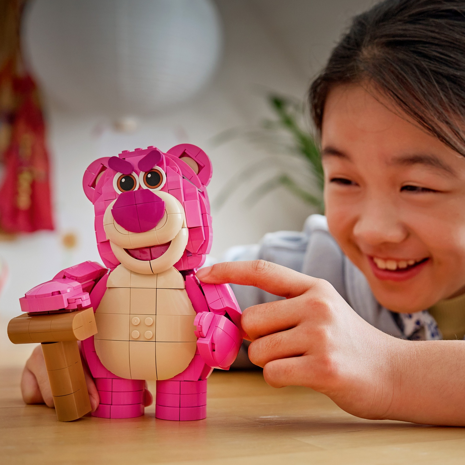 Una ragazza tocca un orso Lego rosa con un martello.