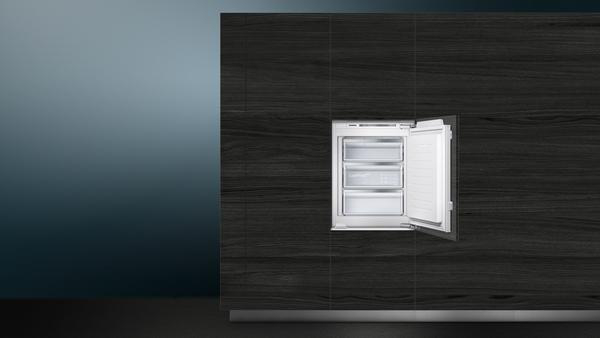 Einbaukühlschrank mit geöffneter Tür, drei Schubladen sichtbar, vor dunklem Holzdekor.