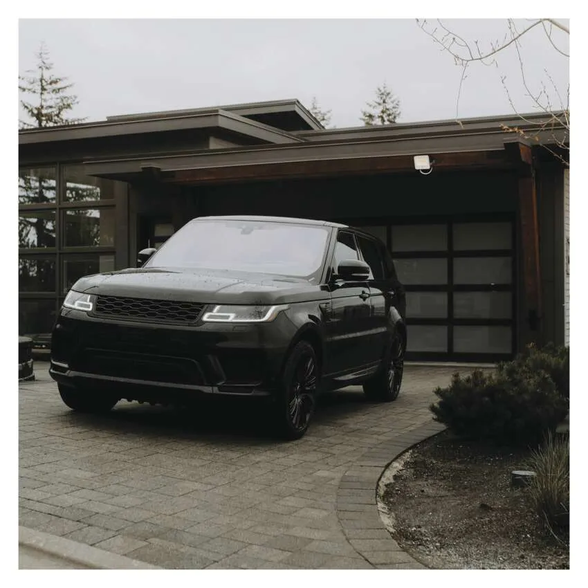 Egy fekete Range Rover áll egy modern ház előtt, garázskapuval, térkövezett felhajtón.