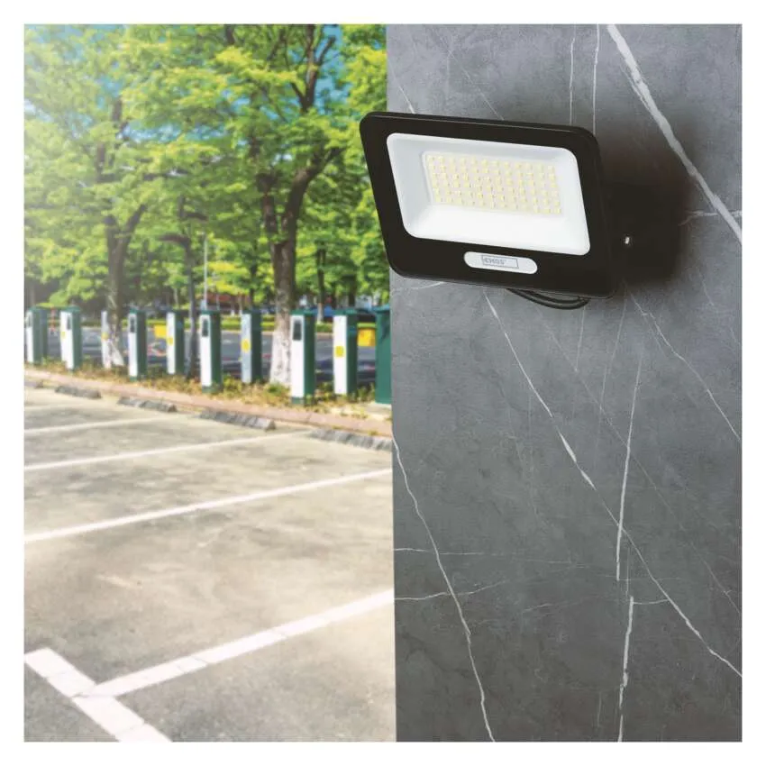 Egy fekete LED-es reflektor egy szürke márványoszlopra van szerelve, parkoló és fák a háttérben.