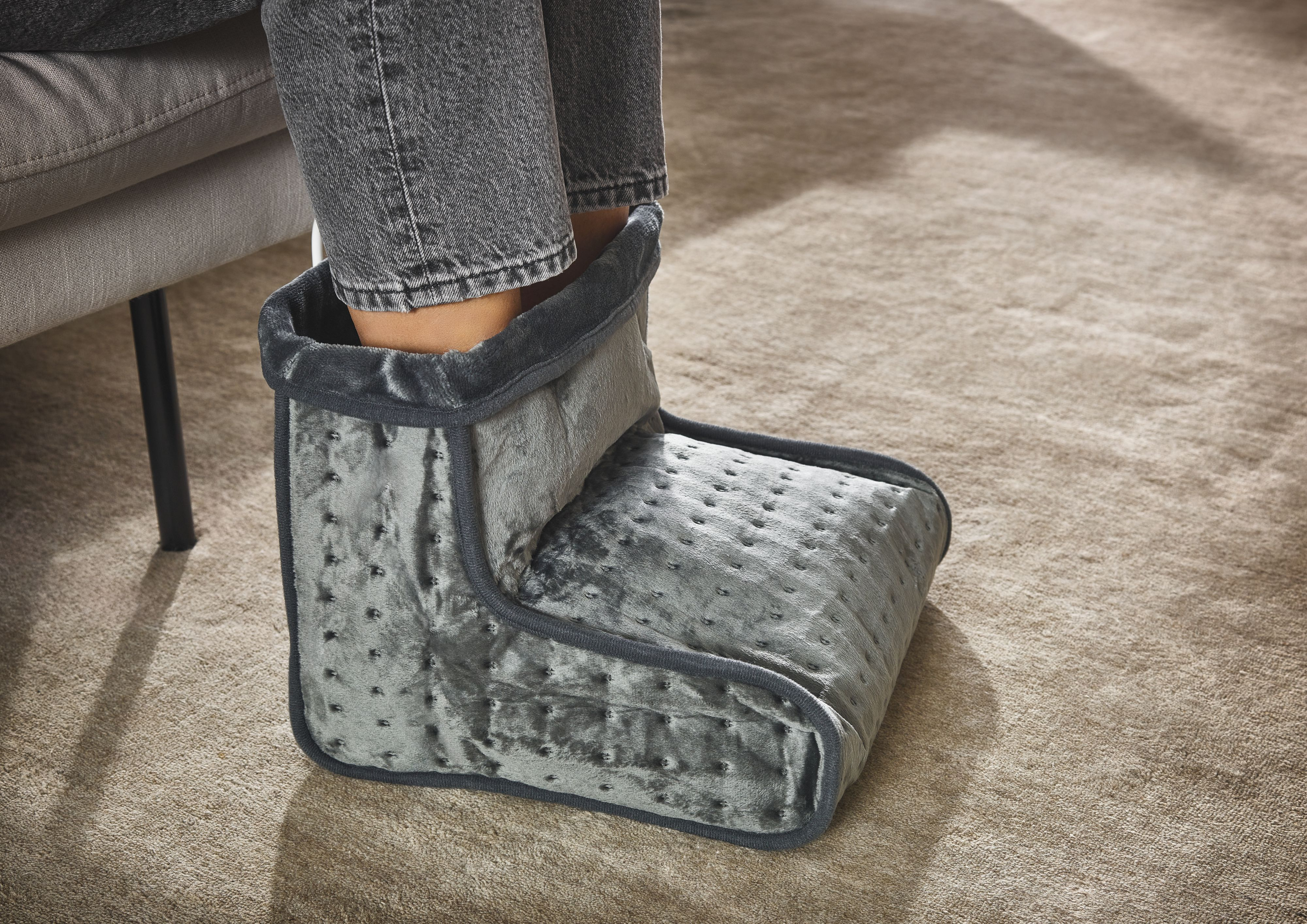 Grauer Heizschuh aus Velours mit kleinen Punkten auf einem beigen Teppich.