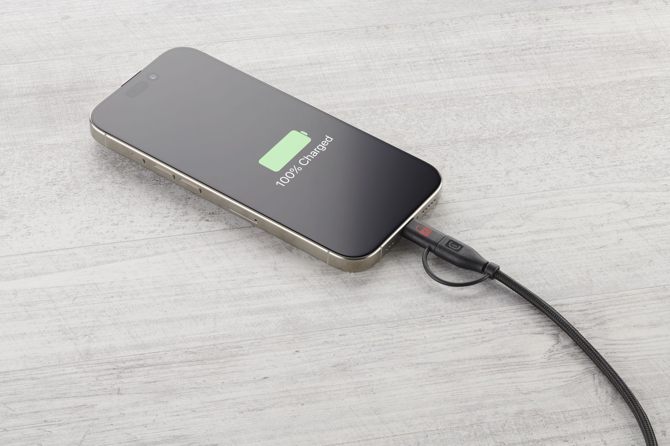 Un smartphone con 100% de carga conectado a un cable de carga negro.