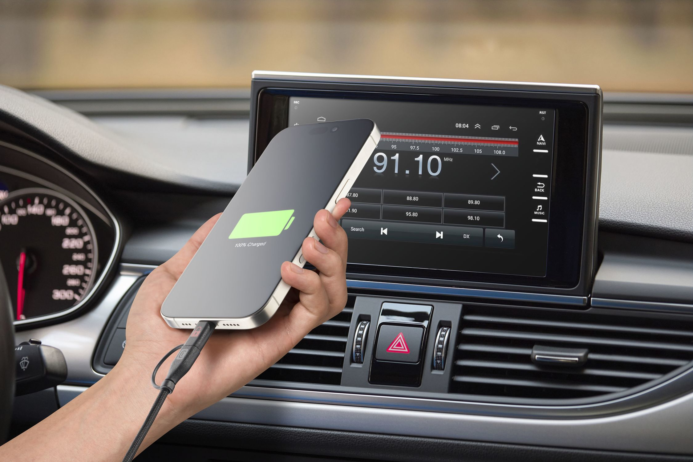 Una mano carga un teléfono en un coche, mostrando 100% cargado.