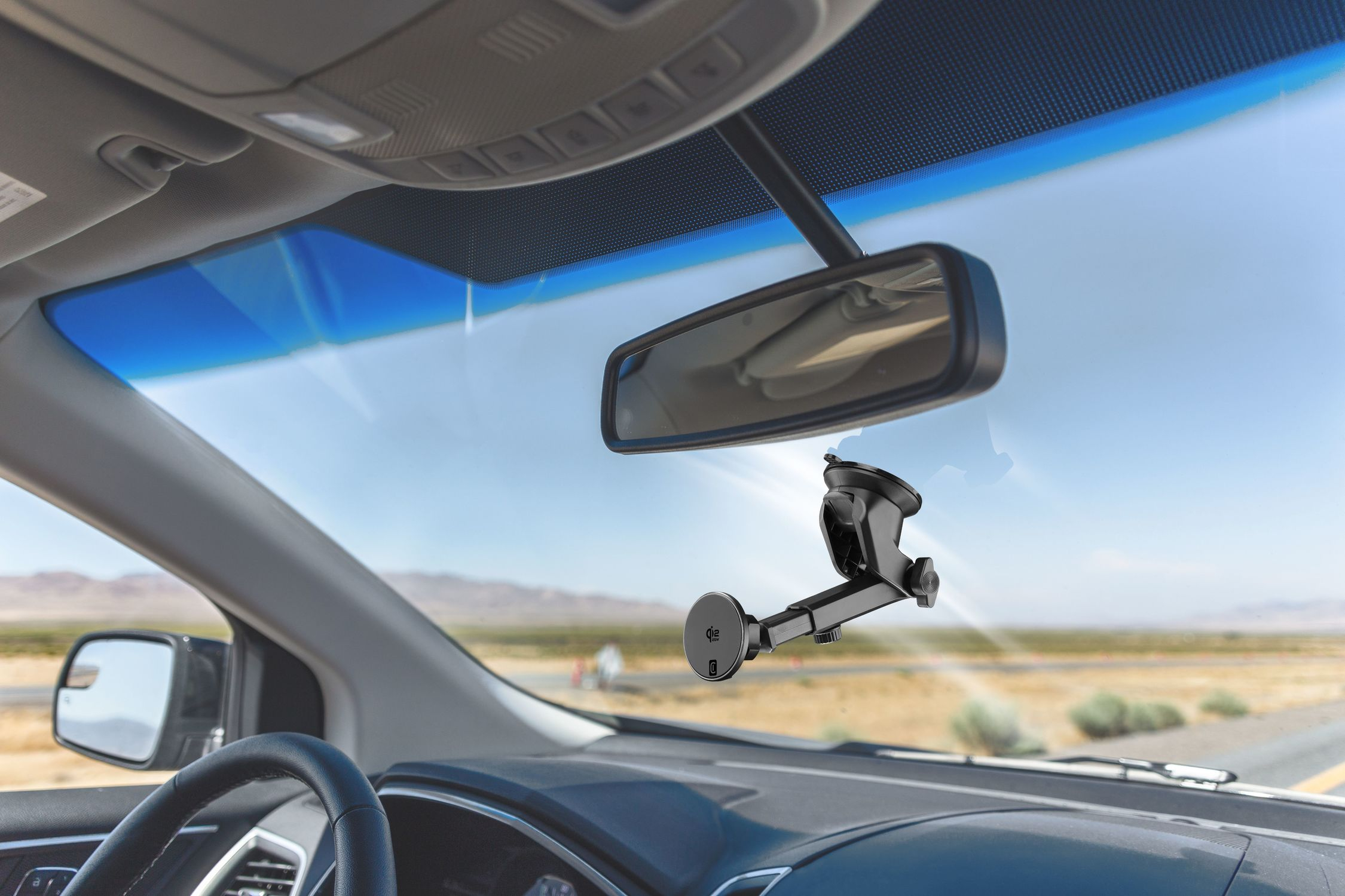 Soporte negro para teléfono con ventosa en parabrisas de coche, paisaje desértico fuera.