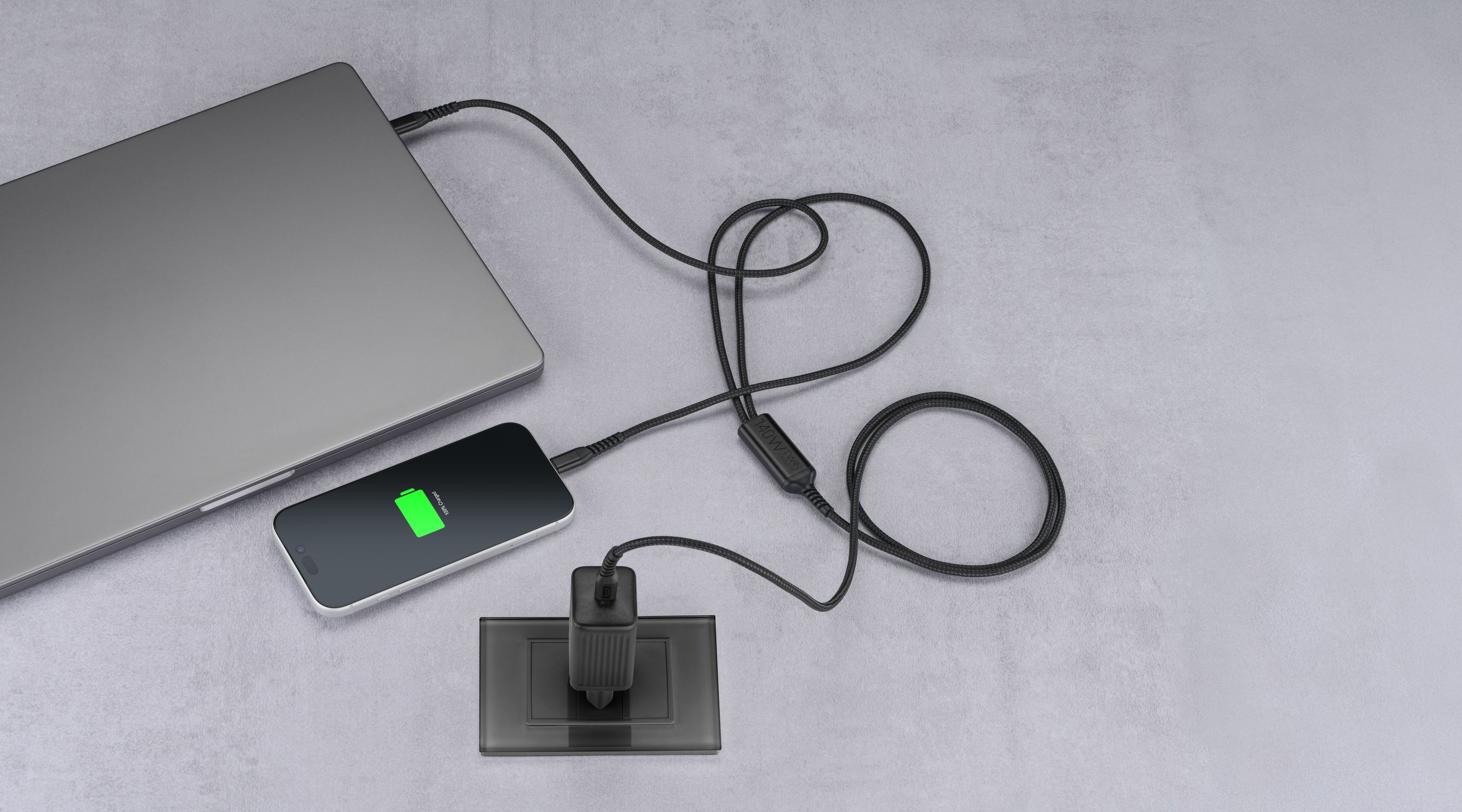 Un portátil, un smartphone y un cargador están conectados sobre una superficie gris.