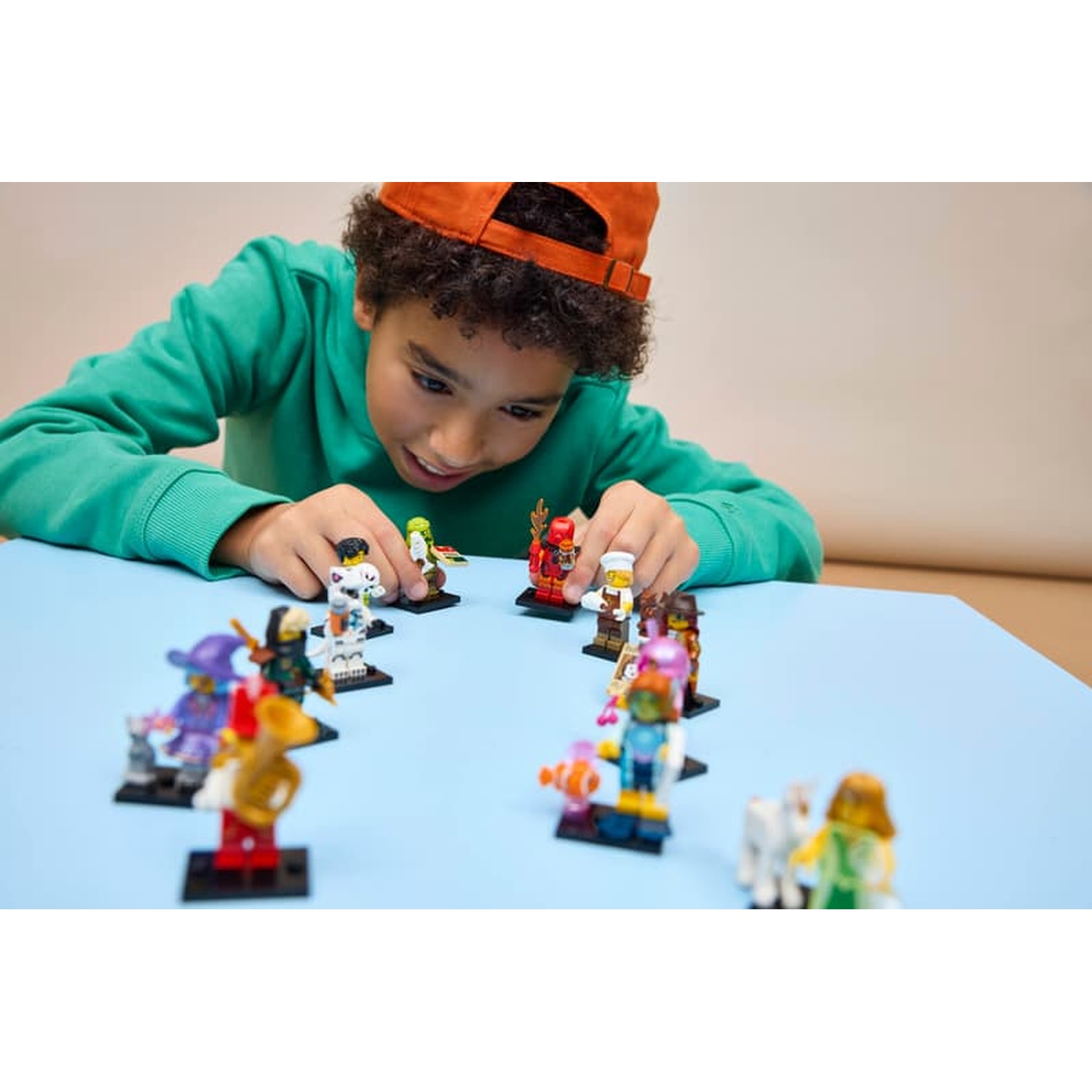 A boy with an orange cap plays with Lego figures on a blue table.