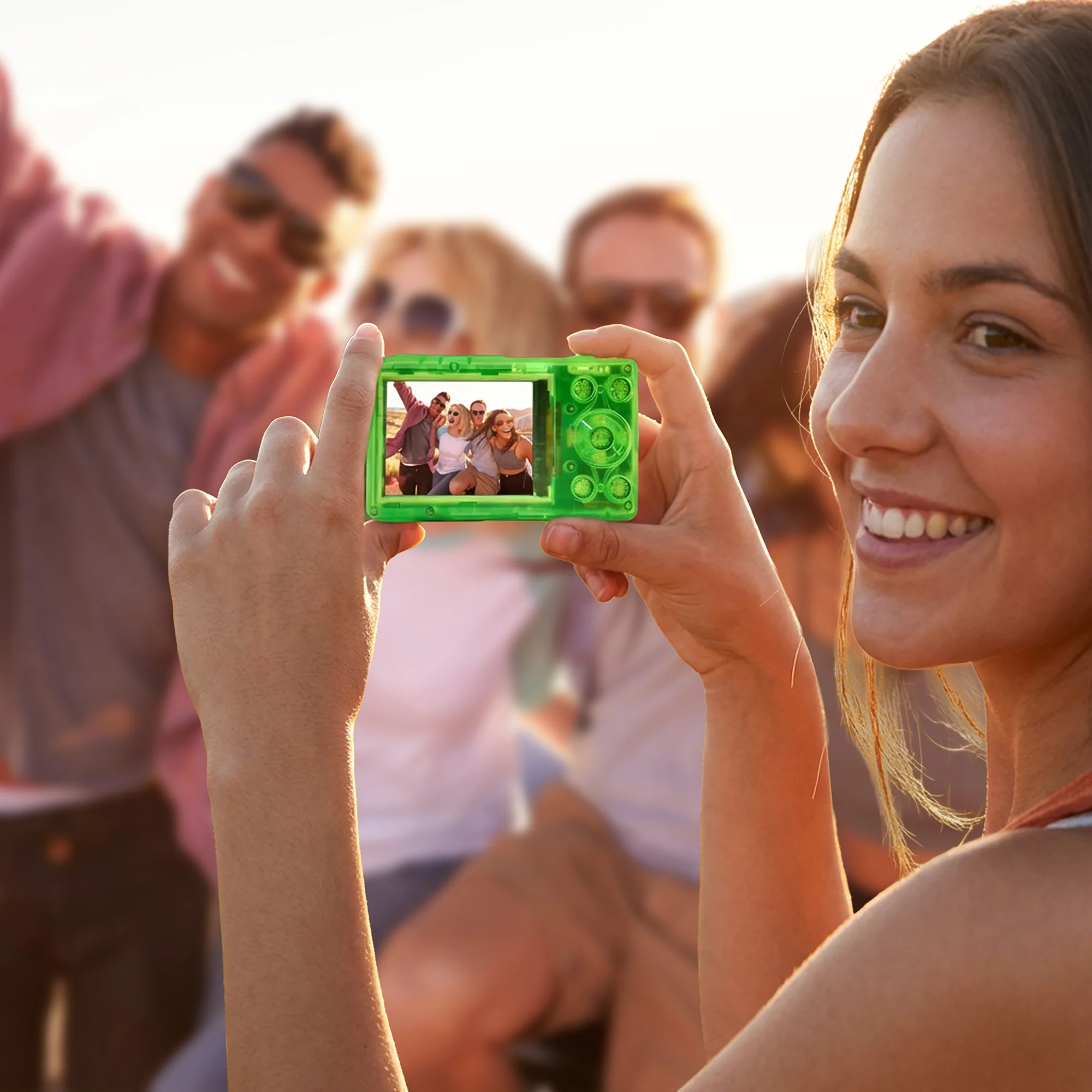 Eine Frau fotografiert mit einer grünen Kamera eine Gruppe lachender Freunde im Freien.