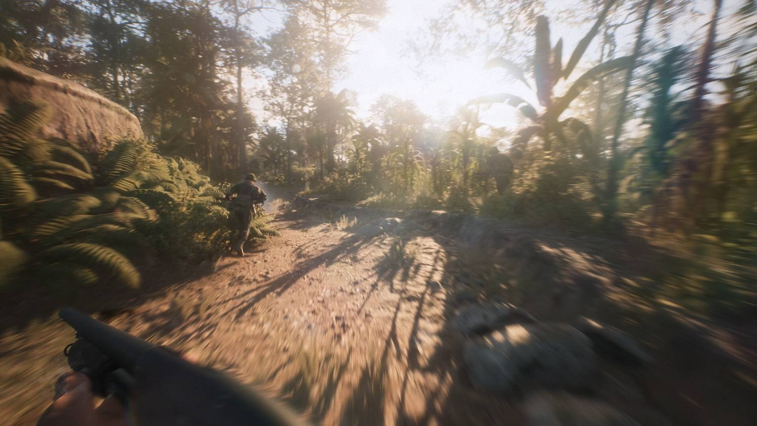 Soldados caminan por un sendero de tierra a través de una jungla soleada con follaje y árboles exuberantes.