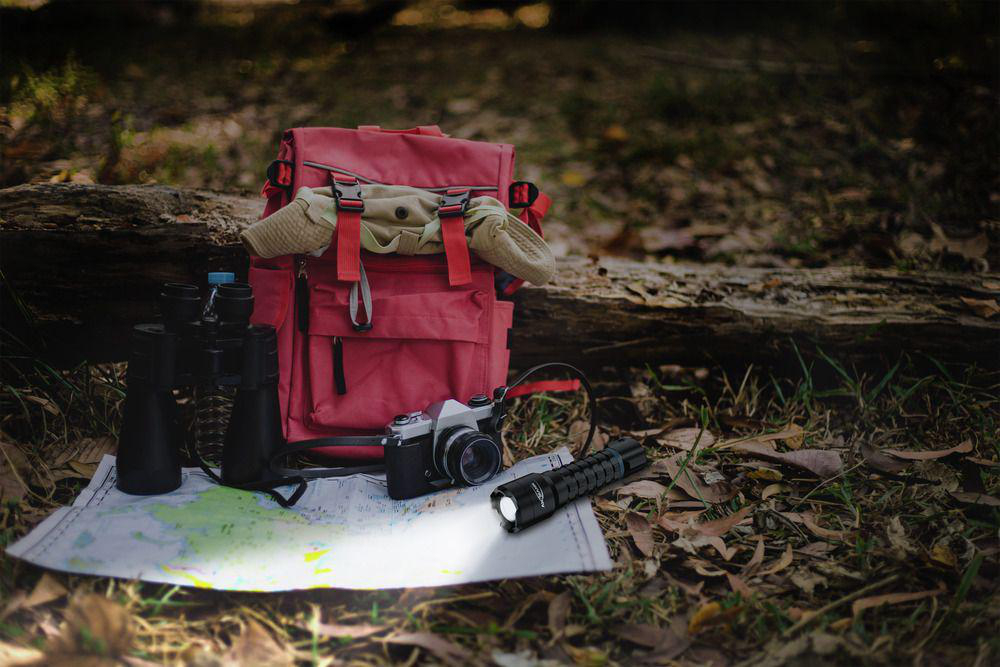 Roter Rucksack, Fernglas, Kamera und Taschenlampe auf Karte im Wald.