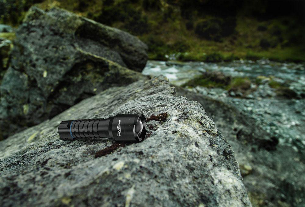 Eine schwarze Taschenlampe liegt auf einem Felsen neben einem Bach.