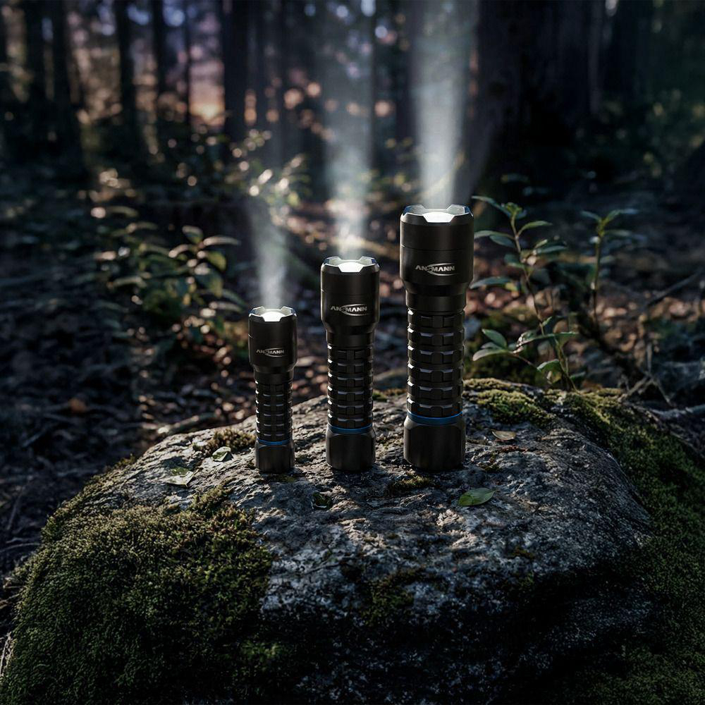 Drei schwarze Taschenlampen unterschiedlicher Größe stehen auf einem moosigen Felsen im Wald.