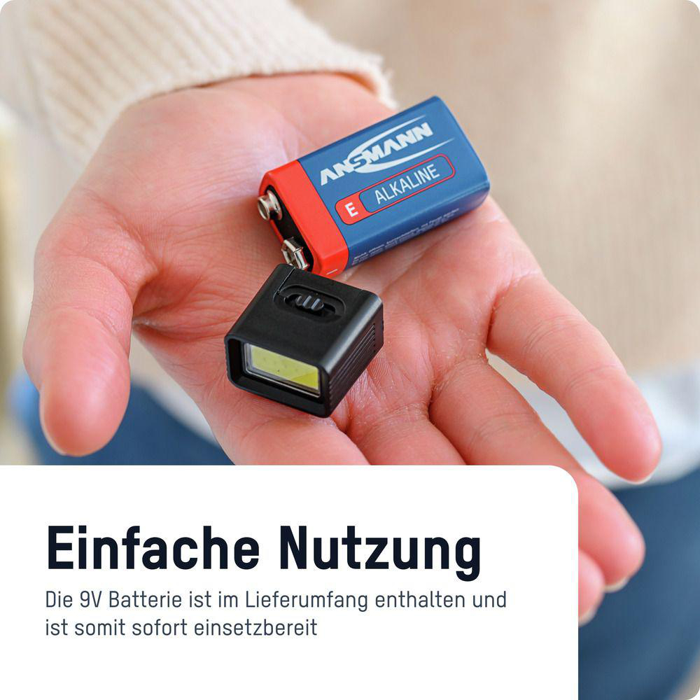 Eine Hand hält eine 9V ANSMANN Batterie und einen kleinen schwarzen LED-Anhänger.