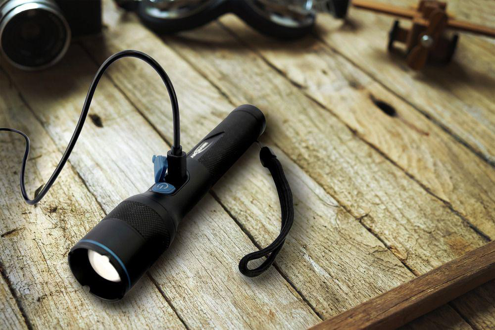 Eine schwarze Taschenlampe mit blauem Knopf lädt auf einem Holztisch.