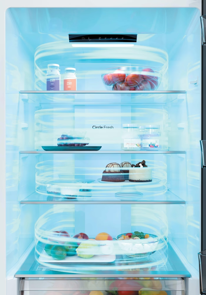 Hűtőszekrény belseje: joghurt, paradicsomos tál, sütemények, gyümölcsök és saláta.