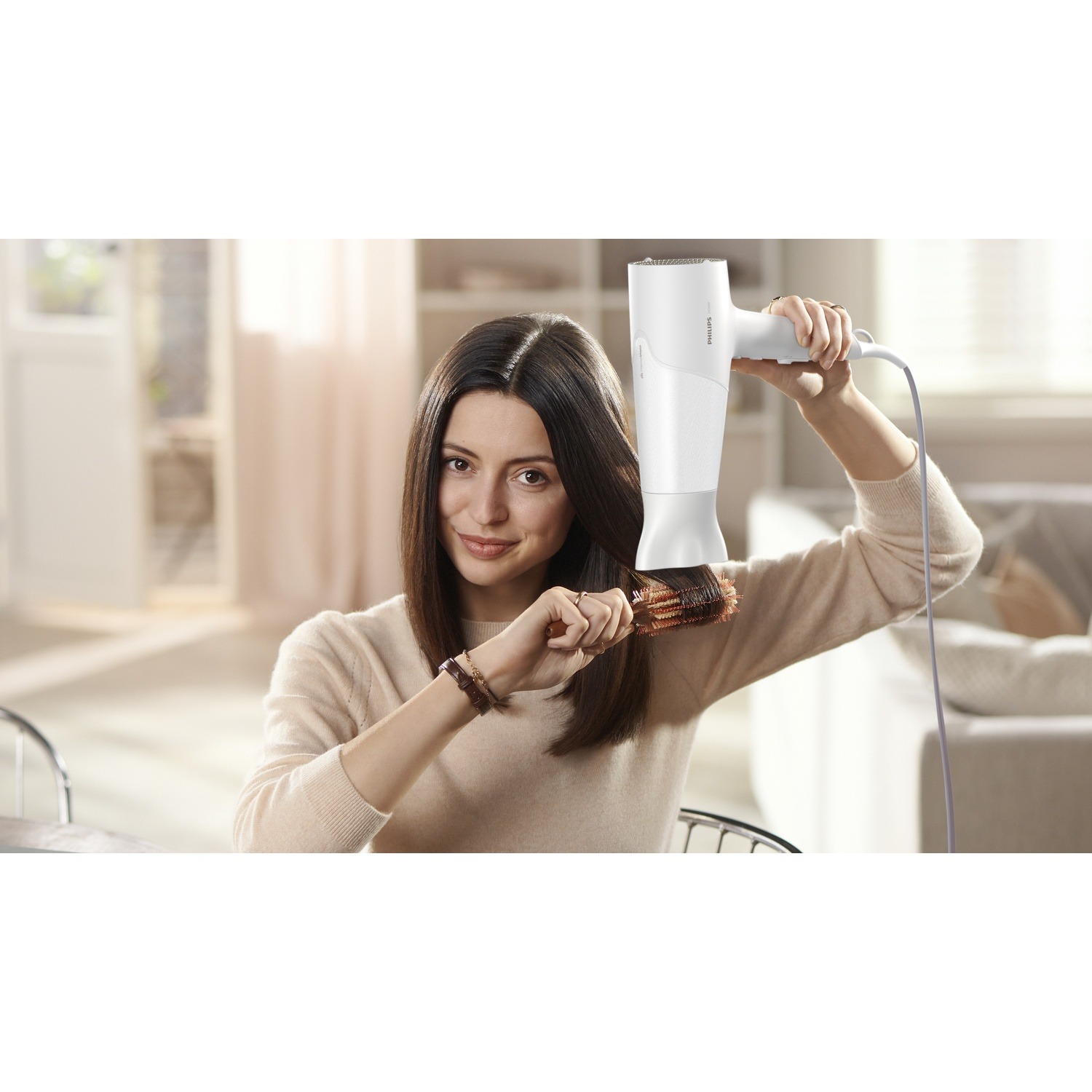 Een vrouw droogt haar haar met een witte föhn en een ronde borstel.