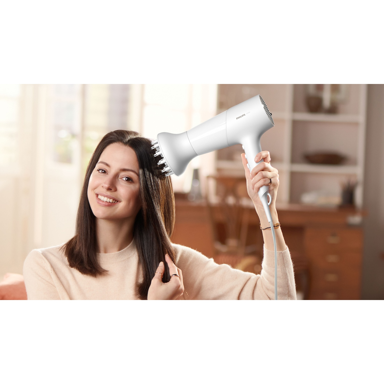 Een vrouw droogt haar donkere haar met een witte Philips haardroger met diffuser.