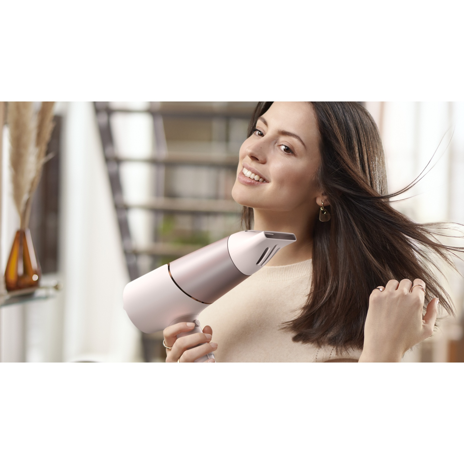 Een vrouw droogt haar bruine haar met een roségouden föhn in een lichte kamer.