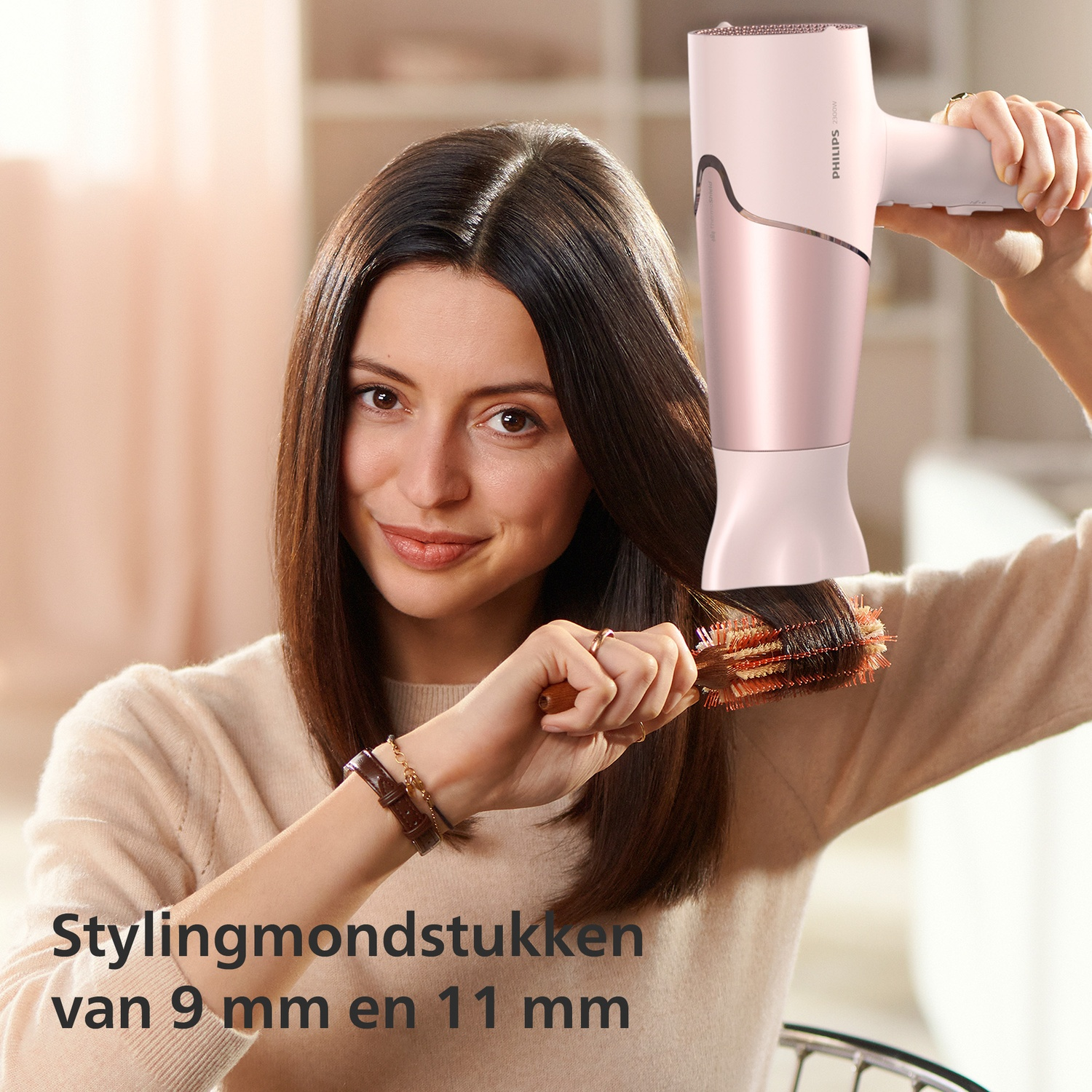 Vrouw föhnt bruin haar met roze föhn en ronde borstel.