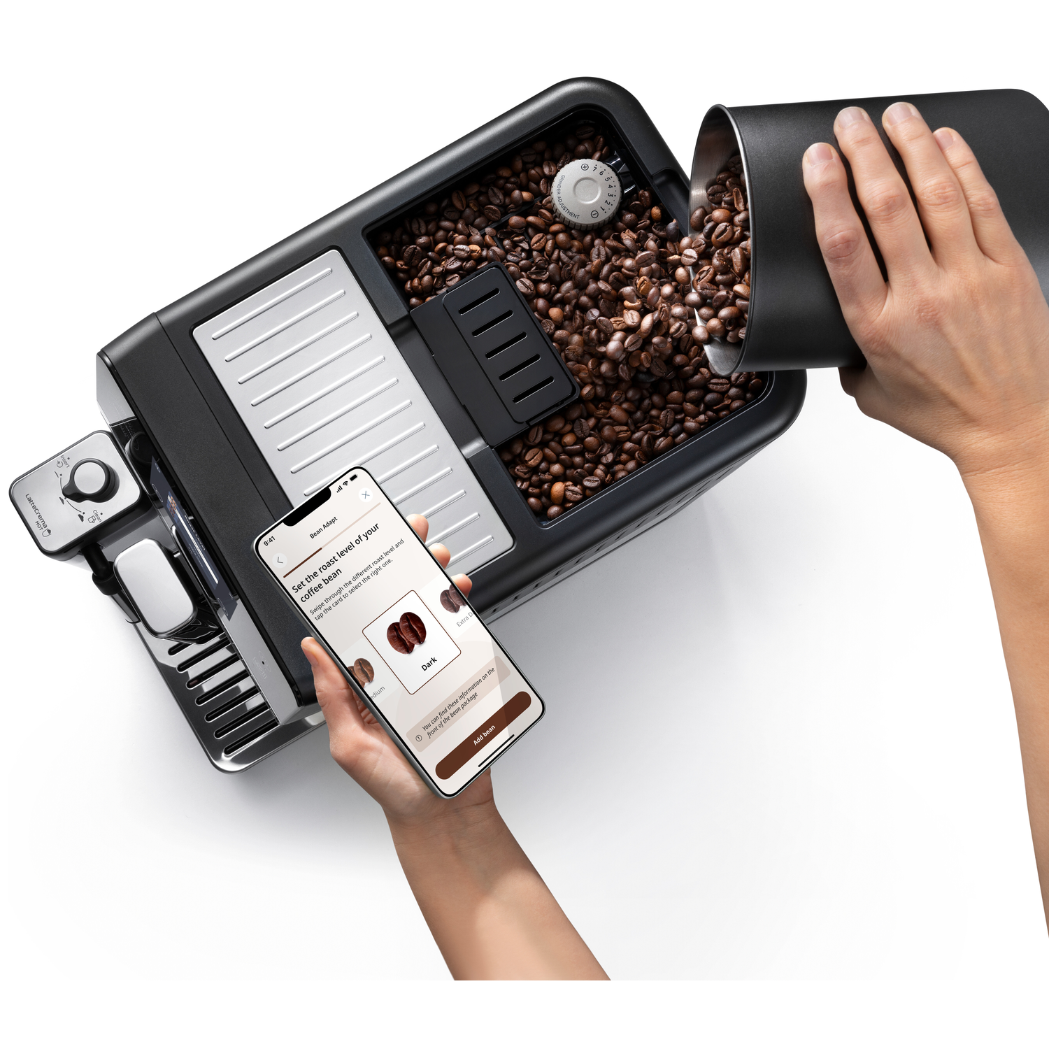 Een hand schenkt koffiebonen in een koffiezetapparaat, terwijl een andere een smartphone vasthoudt.