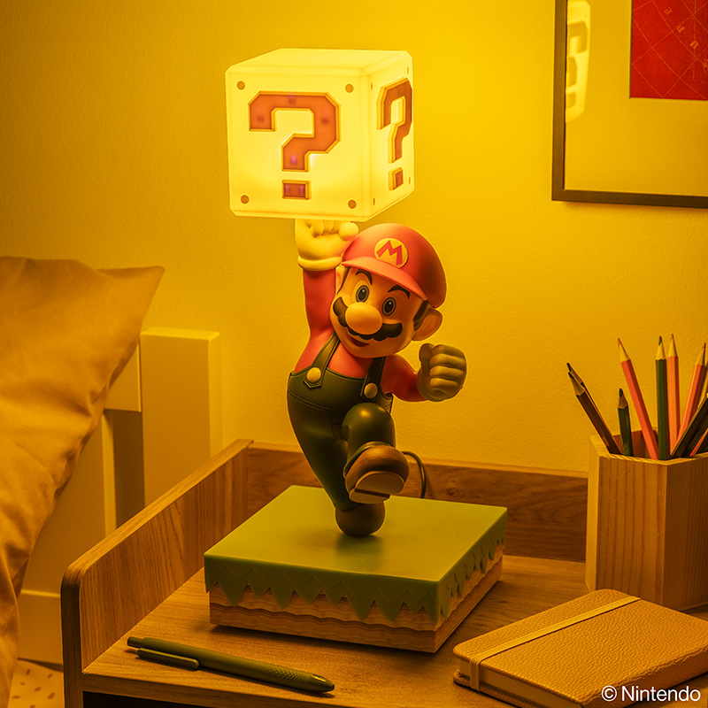 Mario-Figur mit leuchtendem Fragezeichenblock-Lampe auf Holzschreibtisch.