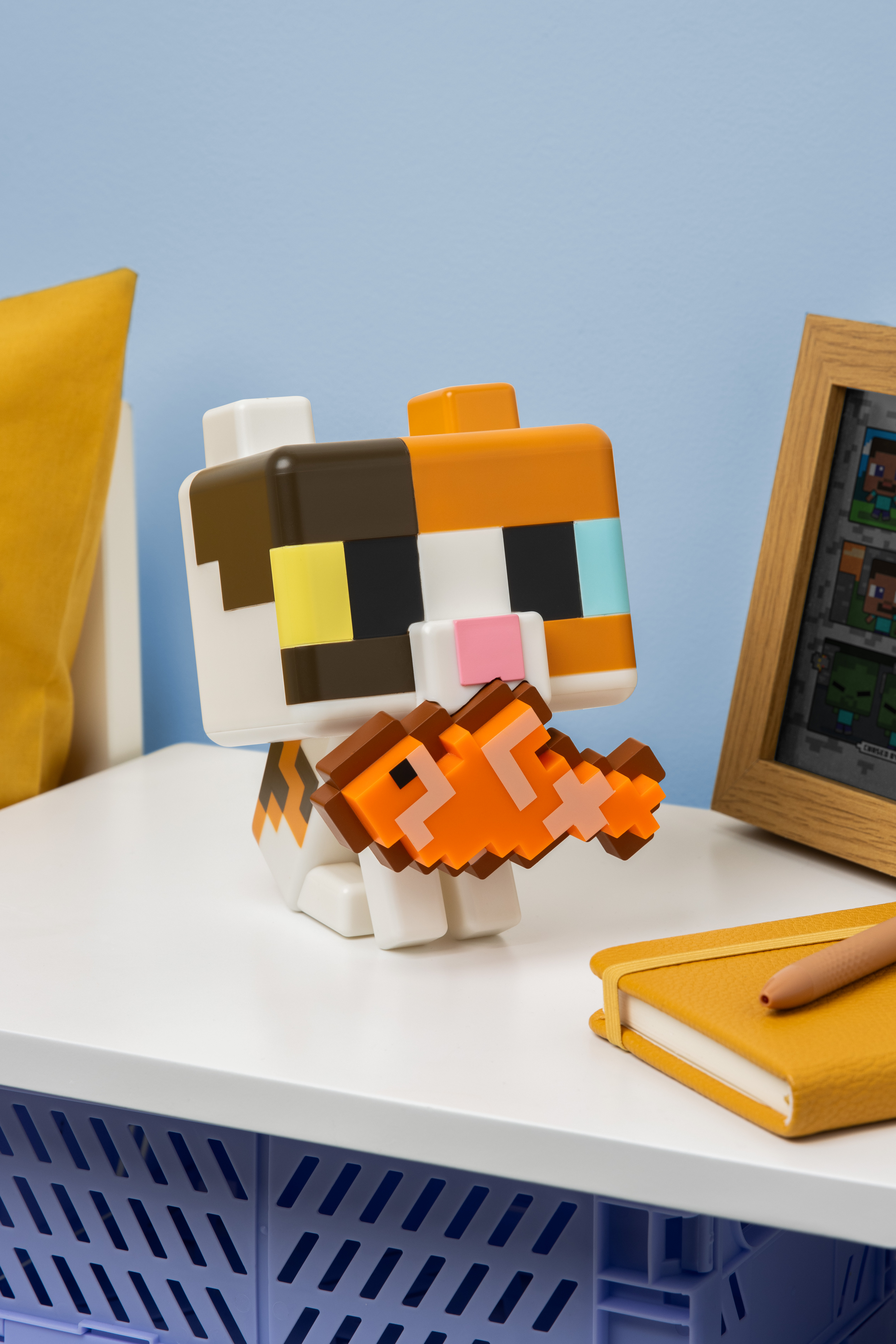 Pixeliger Katzencharakter hält einen orangefarbenen Fisch. Daneben ein Notizbuch.